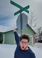 beard brown_hair clothes glasses hair irl open_mouth pointing sign snow street text troon_village // 1790x2456 // 785.1KB